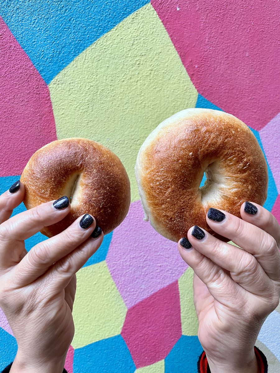 Two bagels held up against a painted wall